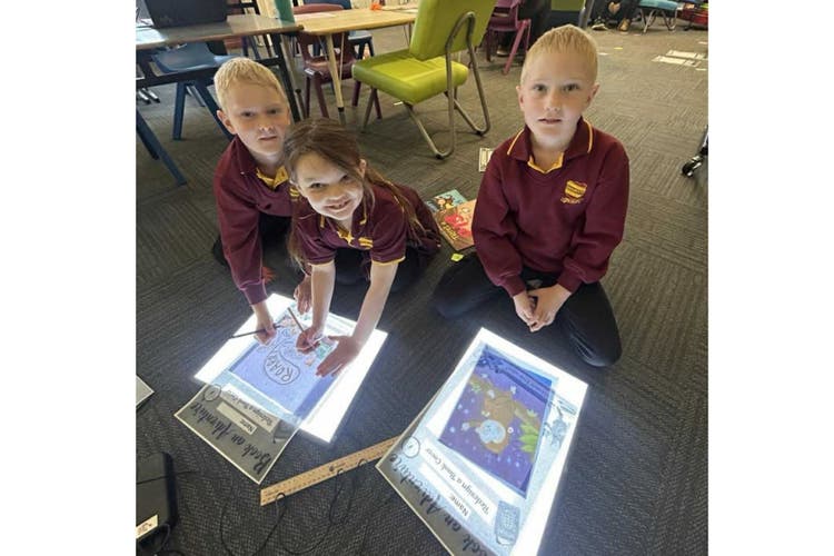 Students sitting on the floor using light boards for drawing