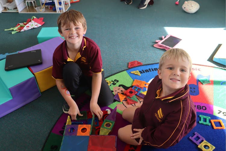 Students sitting on a colourful mat playing with magnetic puzzle pieces.